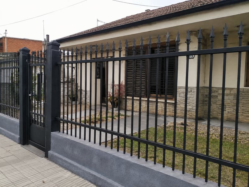 Reja de frente negra con puntas de lanza y puerta de paso, sobre muro bajo