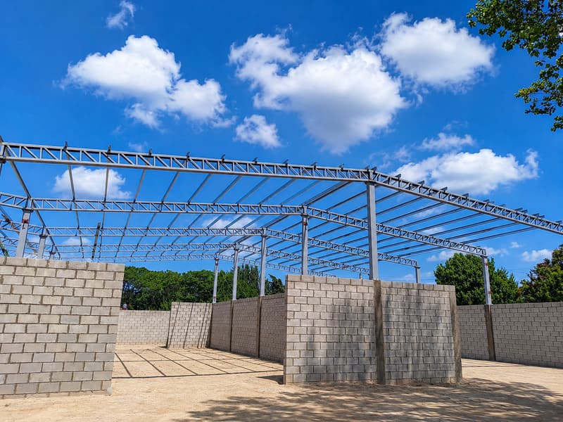 Estructura metálica de un tinglado en obra, con vigas reticuladas sobre columnas y muros de bloque